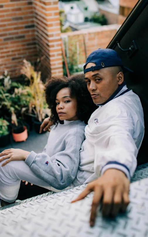 a man and a woman sitting in the back of a truck, a portrait, unsplash, renaissance, wearing a track suit, tessa thompson inspired, daddy/fatherly, promotional image