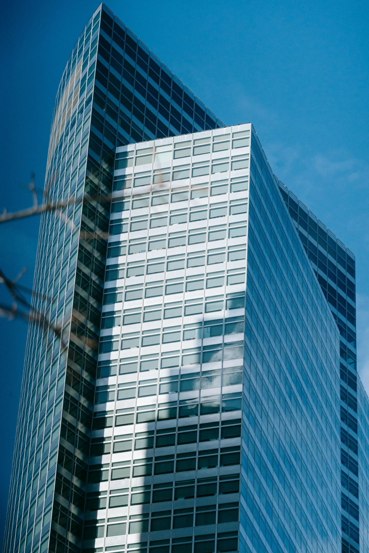 a couple of tall buildings sitting next to each other, an album cover, inspired by Richard Wilson, unsplash, glass face, blue skies, square enix, telephoto shot