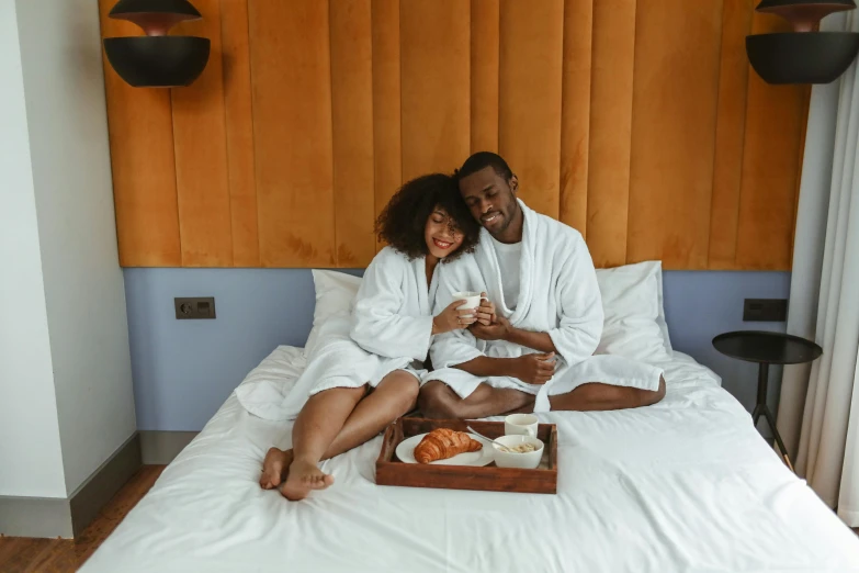 a man and woman sitting on a bed next to each other, pexels contest winner, breakfast, sleek robes, with brown skin, thumbnail