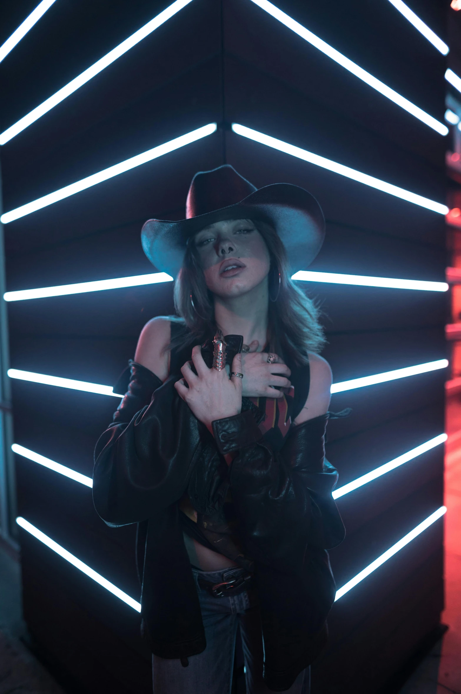 a woman standing in front of a wall with neon lights, an album cover, trending on pexels, dressed as a western sheriff, charli bowater, in a black room, performing a music video