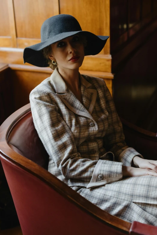 a woman sitting in a chair wearing a hat, inspired by Pruett Carter, unsplash, renaissance, wearing wool suit, gentleman's club lounge, thumbnail, 1 9 5 0 s style