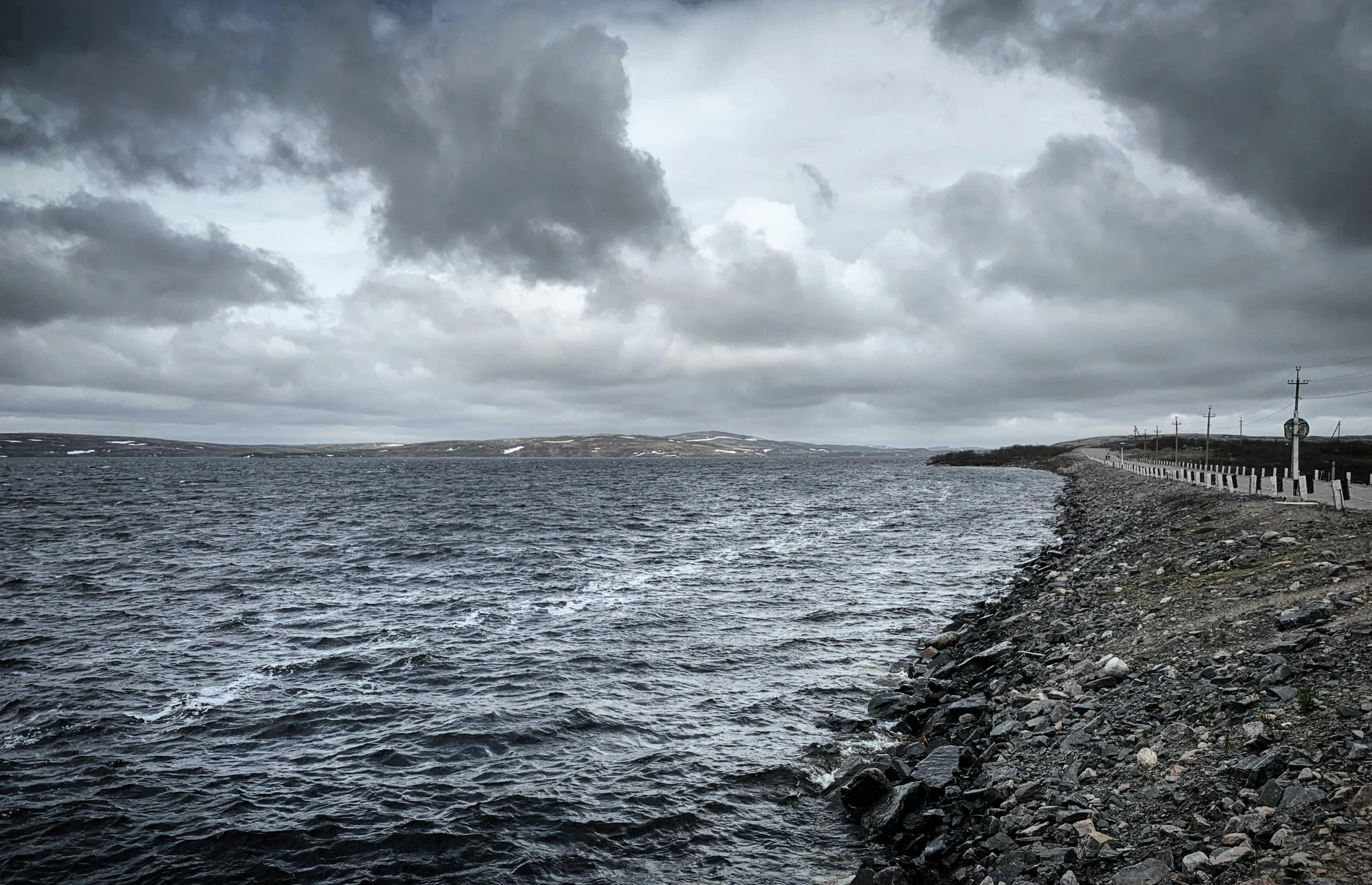 a large body of water under a cloudy sky, by Hallsteinn Sigurðsson, pexels contest winner, hurufiyya, in the distance is a rocky hill, grey, natural stone road, panoramic