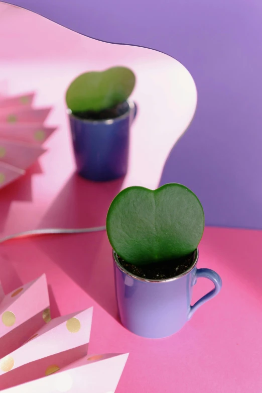 a cup of coffee sitting on top of a pink table, inspired by Yves Klein, patchy cactus, hearts, product display photograph, green plant