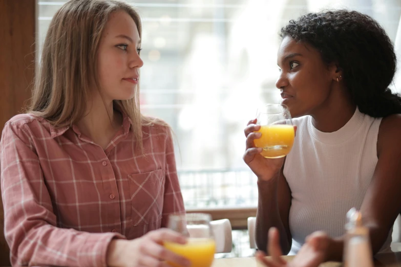 two women sitting at a table drinking orange juice, pexels, varying ethnicities, looking at each other mindlessly, amanda lilleston, teenage girl