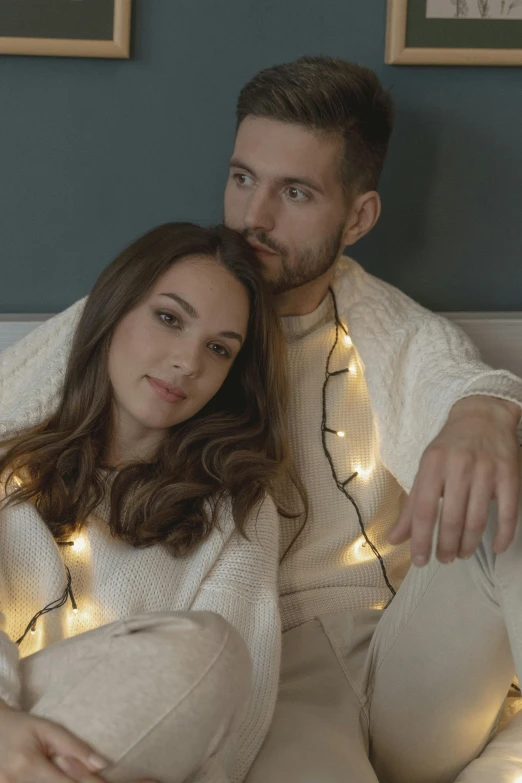 a man and a woman sitting on a bed, christmas lights, wearing a white sweater, profile image, light clothing