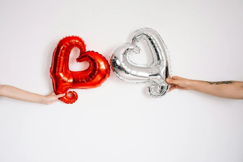 two people holding red and silver balloons in the shape of a heart, pexels, hurufiyya, background image, product shot, silver red, foil