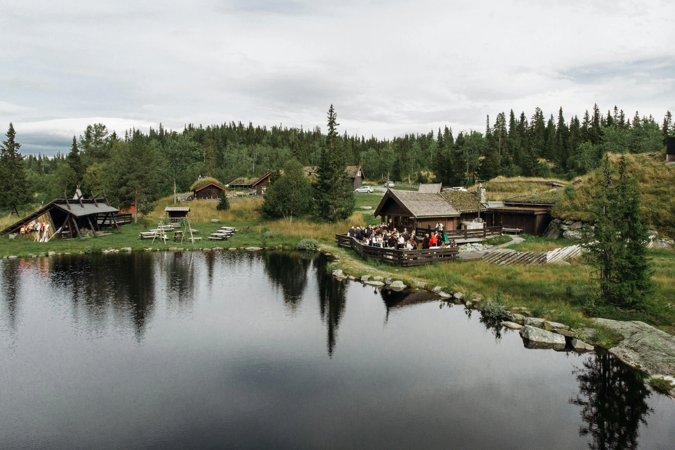 a group of people standing next to a body of water, by Jaakko Mattila, hurufiyya, cottages, a high angle shot, from the distance, wedding