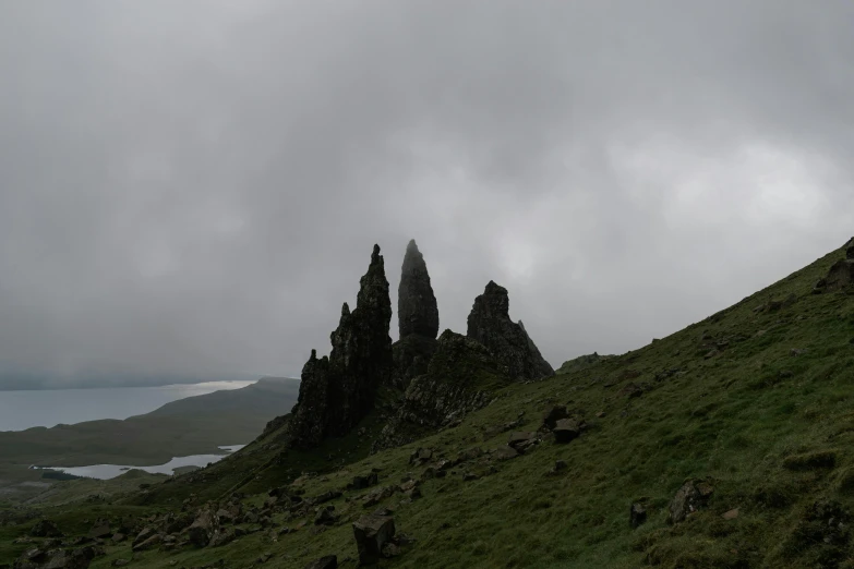 a group of rocks sitting on top of a lush green hillside, by Andrew Allan, pexels contest winner, romanticism, tall stone spires, grey sky, skye meaker, 2000s photo