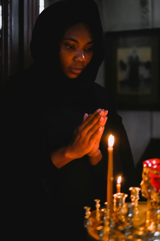 a woman standing in front of a lit candle, by Emanuel Witz, pexels, hurufiyya, wearing a black robe, praying, african ameera al taweel, center of image