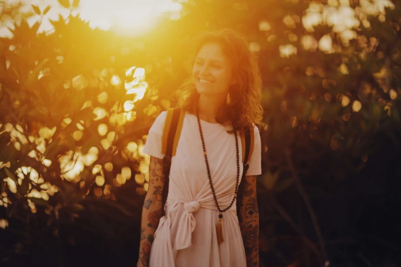 a woman standing in front of a tree at sunset, pexels contest winner, with tattoos, warm smile, hazy light rays, justina blakeney