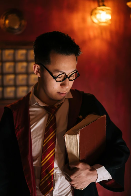 a man in a suit and tie holding a book, an album cover, inspired by Feng Zhu, pexels contest winner, magical realism, hogwarts gryffindor common room, asian man, dressed as a wizard, reading glasses