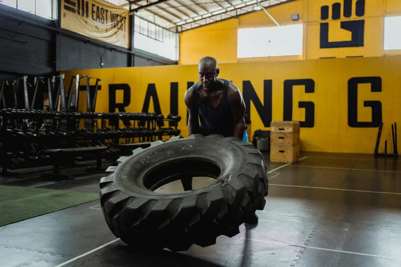 a man holding a large tire in a gym, a portrait, pexels contest winner, yellow and charcoal, avatar image, ground level shot, malaysian