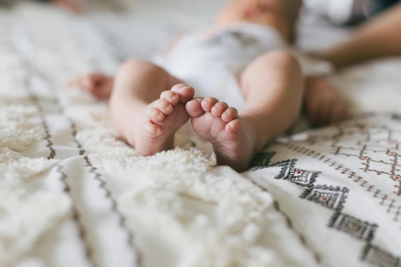 a close up of a baby's feet on a bed, by Will Ellis, trending on pexels, full body image, beautiful high resolution, lying down, covered with blanket
