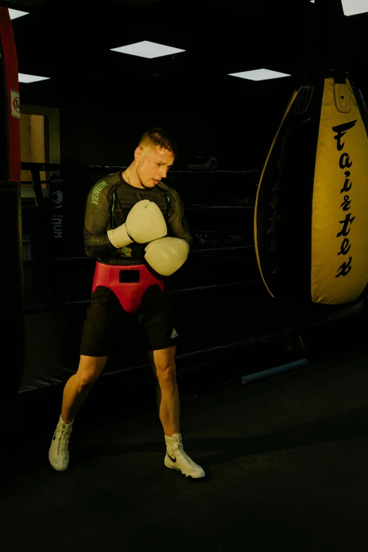 a man standing next to a punching bag, by Tom Bonson, happening, chest guard, liam brazier, forward facing, lights on