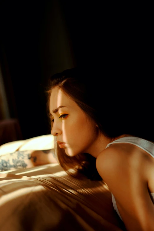 a woman laying on top of a bed next to a window, inspired by Elsa Bleda, trending on pexels, photorealism, glowing yellow face, tattooed, kiko mizuhara, discreet lensflare