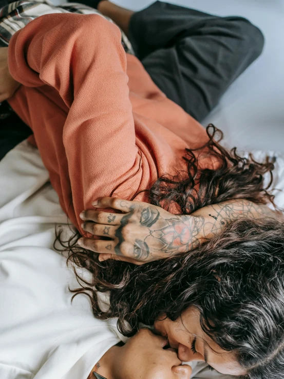 a woman laying on top of a bed next to a man, a tattoo, inspired by Elsa Bleda, trending on pexels, messy hair bedhead, tattoo sleeve on her right arm, with his hands in his hair, zoomed out