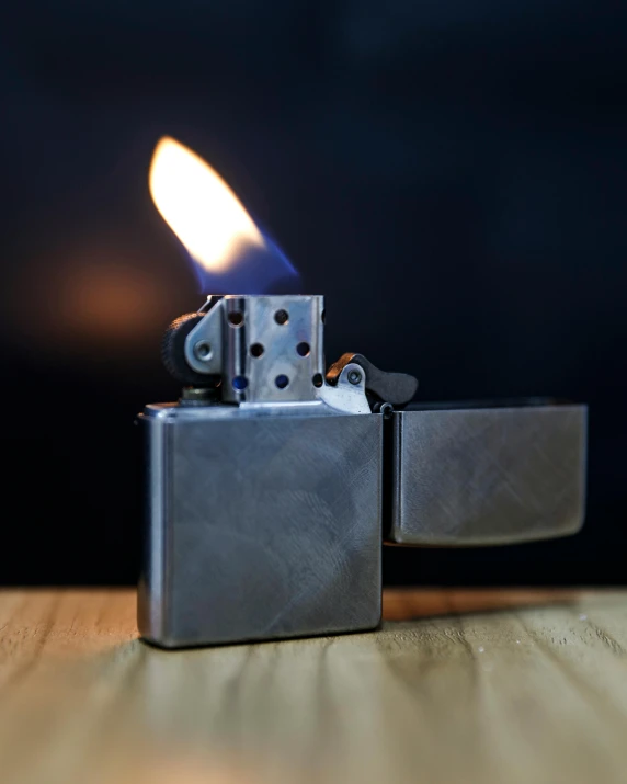 a lighter sitting on top of a wooden table, gunmetal grey, bathed in the the glow of a fire, on grey background, product shot