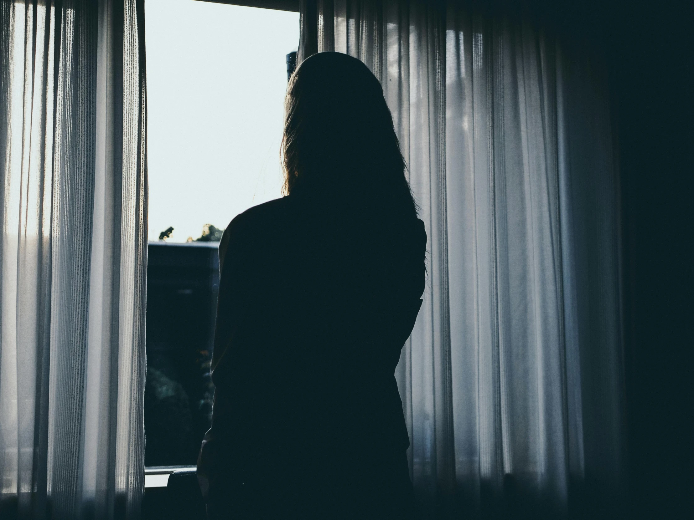 a silhouette of a woman standing in front of a window, instagram photo, she's sad, dark bedroom, woman