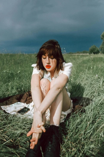 a woman sitting on top of a lush green field, an album cover, unsplash, brown hair and bangs, very pale skin, lipstick, white sky
