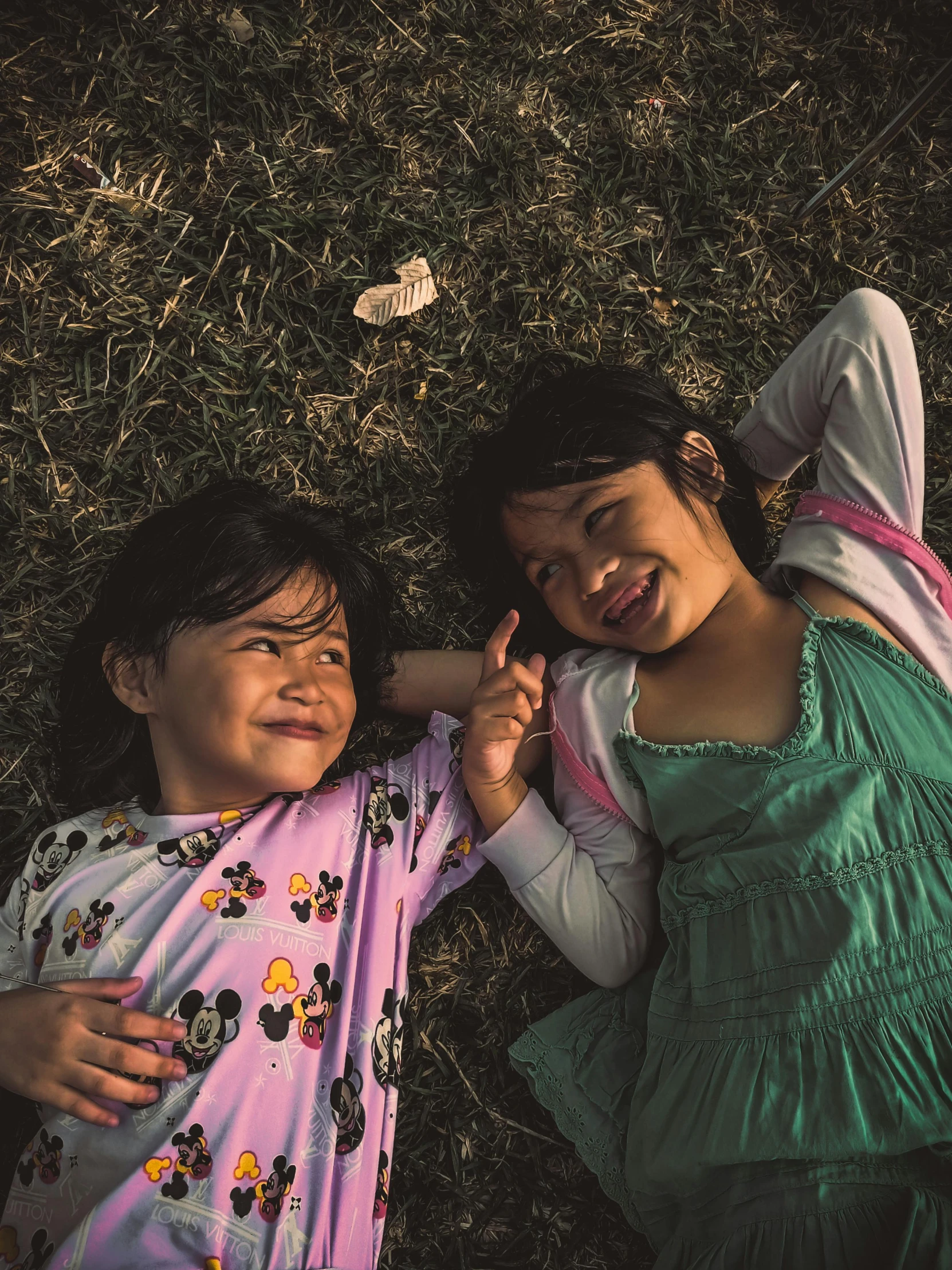 a couple of young girls laying on top of a grass covered field, by Elsa Bleda, pexels contest winner, incoherents, happy kid, 1970s philippines, smiling at each other, 15081959 21121991 01012000 4k