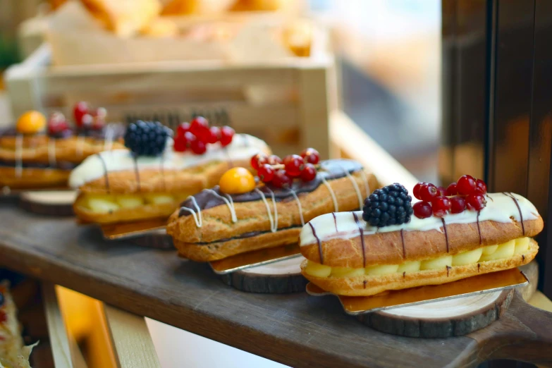 a row of pastries sitting on top of a wooden shelf, inspired by Richmond Barthé, unsplash, hurufiyya, sea of parfait, al fresco, chaumet style, on a wooden tray