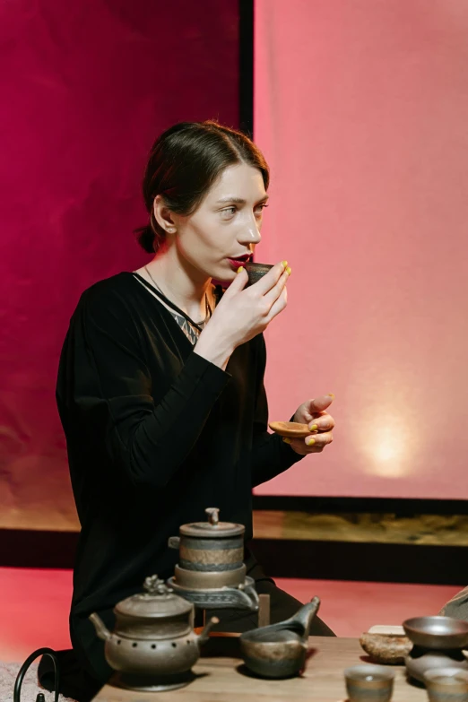 a woman standing in front of a table full of teapots, inspired by Georges de La Tour, unsplash, modernism, woman smoking cigarette, carice van houten, holding flask in hand, performance