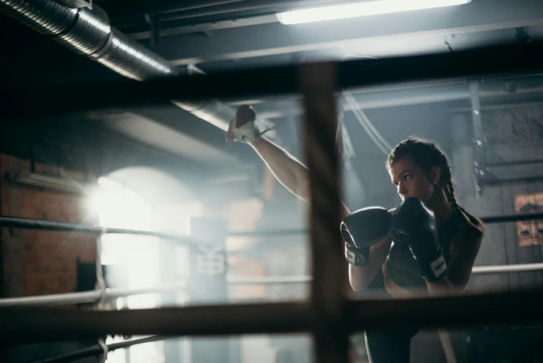 a woman standing in the middle of a boxing ring, by Anna Findlay, pexels contest winner, woman in a dark factory, manuka, in a gym, punching in a bag