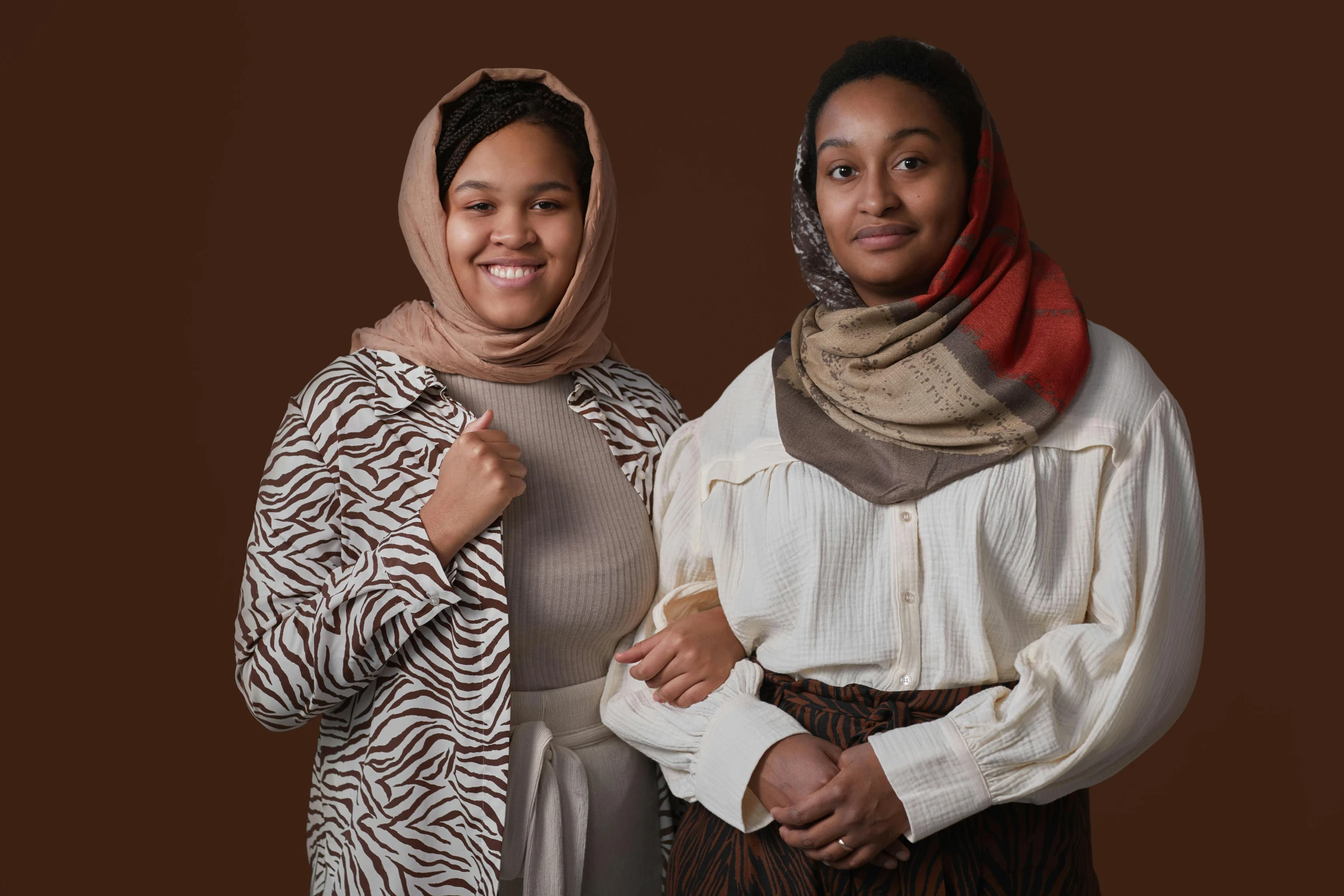 a couple of women standing next to each other, hurufiyya, brown colours, wearing a scarf, photo from a promo shoot, modest!