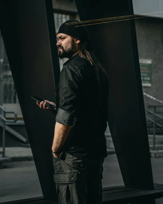 a man standing in front of a window holding a tablet, inspired by Carlo Mense, pexels contest winner, modernism, in a dark space mercenary outfit, black steel buildings, with a beard and a black shirt, cell phone photo