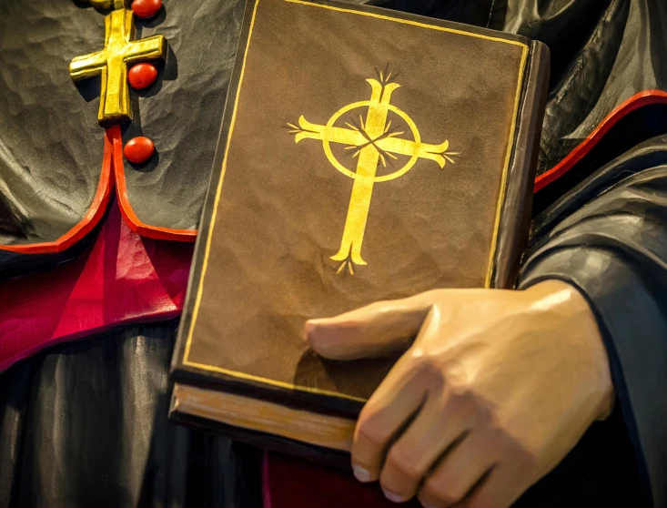 a statue of a man holding a book with a cross on it, a photo, by Julia Pishtar, shutterstock, renaissance, papa emeritus, thumbnail, orthodox icon, leather robes