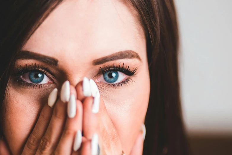 a woman covering her face with her hands, trending on pexels, hurufiyya, large blue eyes, wide nostrils, laser point between the eyes, woman crying