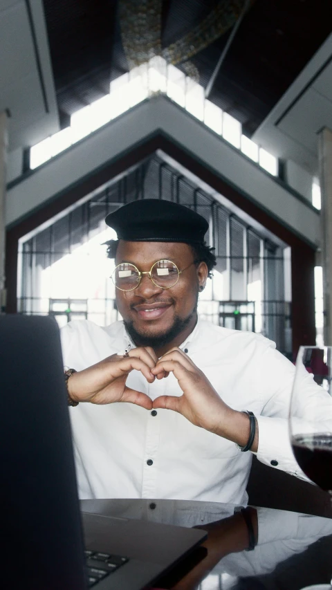 a man sitting at a table in front of a laptop, by Chinwe Chukwuogo-Roy, pexels, renaissance, heart shaped face, cheers, dressed like a cleric, with square glasses
