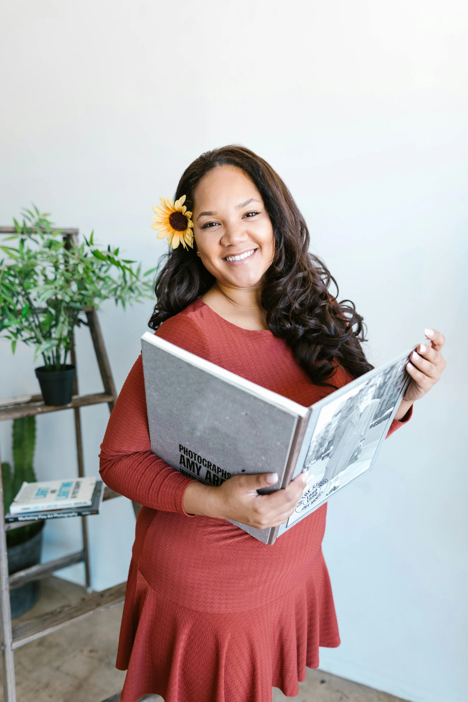 a woman in a red dress holding a magazine, inspired by Daphne Allen, happening, joanna gaines, samoan features, looking towards camera, books and flowers