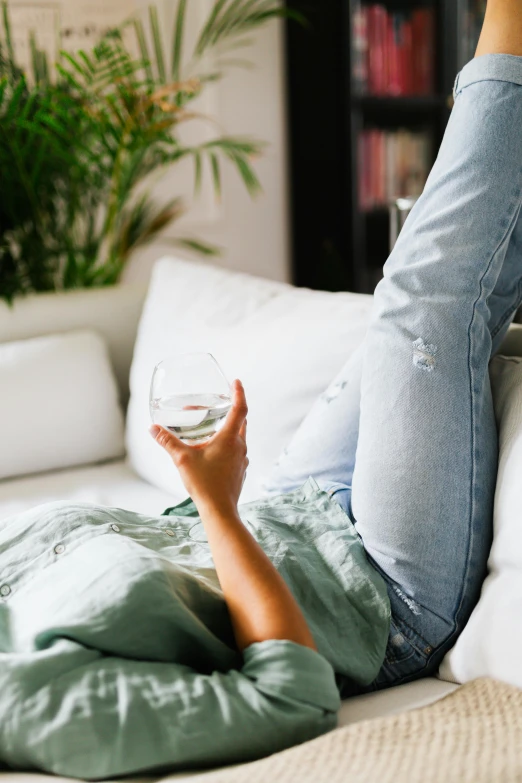 a woman laying on a couch holding a glass of wine, inspired by Constantin Hansen, trending on unsplash, denim, green water, morning detail, sheer fabrics