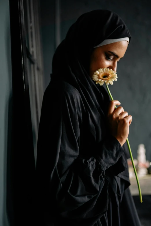 a woman in a black robe holding a flower, by irakli nadar, trending on unsplash, hurufiyya, islamic, pensive expression, indoor picture, 15081959 21121991 01012000 4k