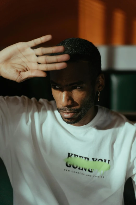 a man that is sitting down with his hands on his head, an album cover, inspired by Barthélemy Menn, trending on pexels, in a dark green polo shirt, intimidating pose, mkbhd, man in white t - shirt