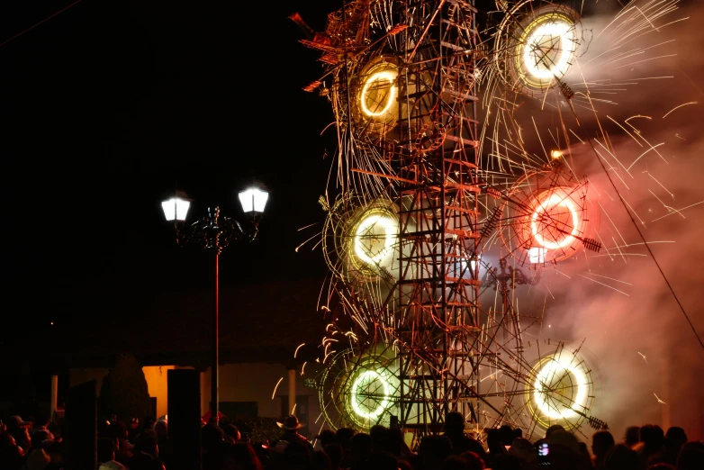 a group of people watching a fireworks display, an abstract sculpture, by Matteo Pérez, pexels contest winner, kinetic art, giant imposing steampunk tower, close up of lain iwakura, square, shot on sony a 7