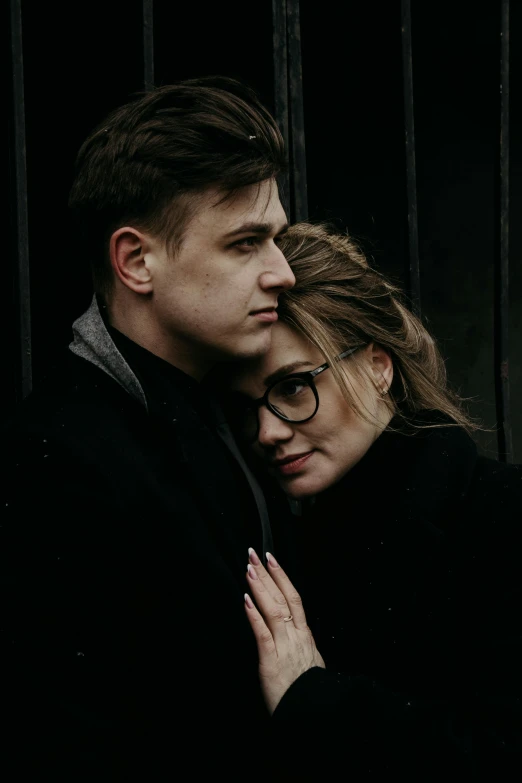 a man and a woman standing next to each other, by Lucia Peka, pexels, wrapped in black, alexey gurylev, with glasses, embraced