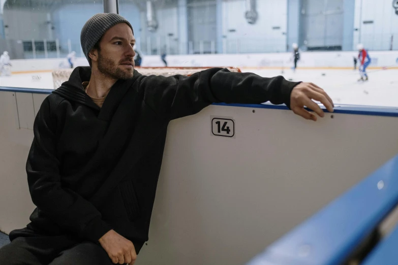 a man sitting on a bench in front of a hockey rink, profile image, sports clothing, paul walker, grey