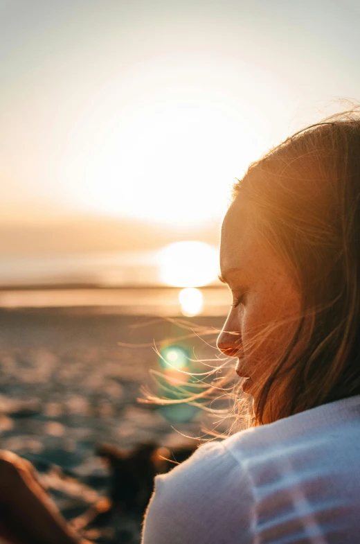 a woman sitting on top of a sandy beach, trending on unsplash, backlit ears, looking off into the sunset, a close up shot, sleepy