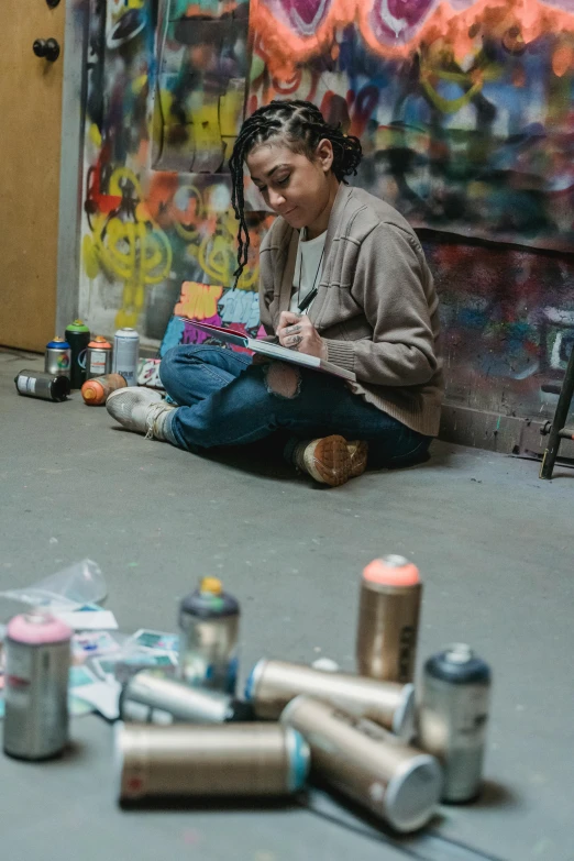 a woman sitting on the floor next to cans of paint, an airbrush painting, process art, studious, in an urban setting, profile image, lesbian art