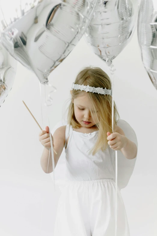 a little girl holding a bunch of silver balloons, inspired by Ida Rentoul Outhwaite, pexels contest winner, wearing angel halo, white room, wearing a headband, holding a white flag