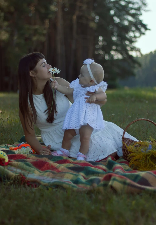 a woman sitting on a blanket holding a baby, pexels contest winner, symbolism, picking flowers, ukrainian girl, square, official screenshot