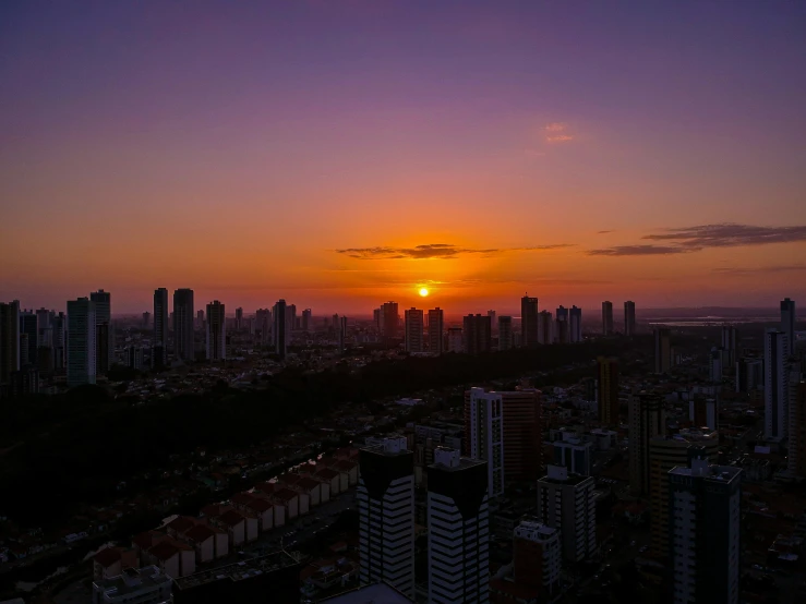 the sun is setting over the city skyline, by Alejandro Obregón, pexels contest winner, carnaval de barranquilla, drone footage, purple sunset, ((sunset))