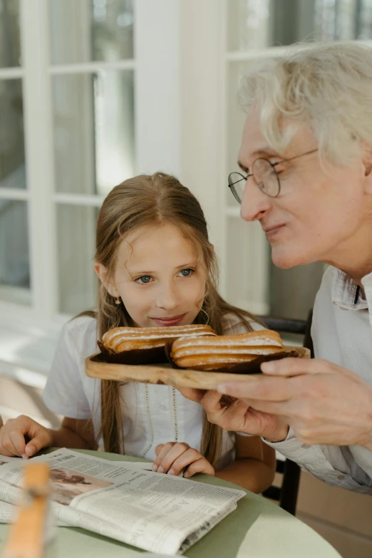 a woman and a little girl sitting at a table with donuts, pexels contest winner, an oldman, gif, gray haired, holding a baguette