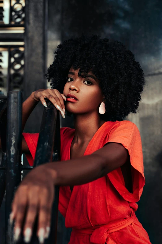 a woman in a red dress leaning on a gate, pexels contest winner, afrofuturism, (dark shorter curly hair), square, black young woman, high resolution image