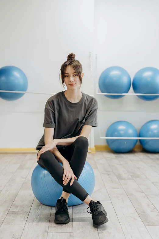 a woman sitting on an exercise ball in a gym, by Adam Marczyński, trending on pexels, portrait sophie mudd, blue and grey, no - text no - logo, standing