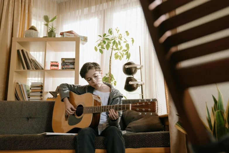 a man sitting on a couch playing a guitar, pexels contest winner, teen boy, slightly sunny, little kid, high quality screenshot