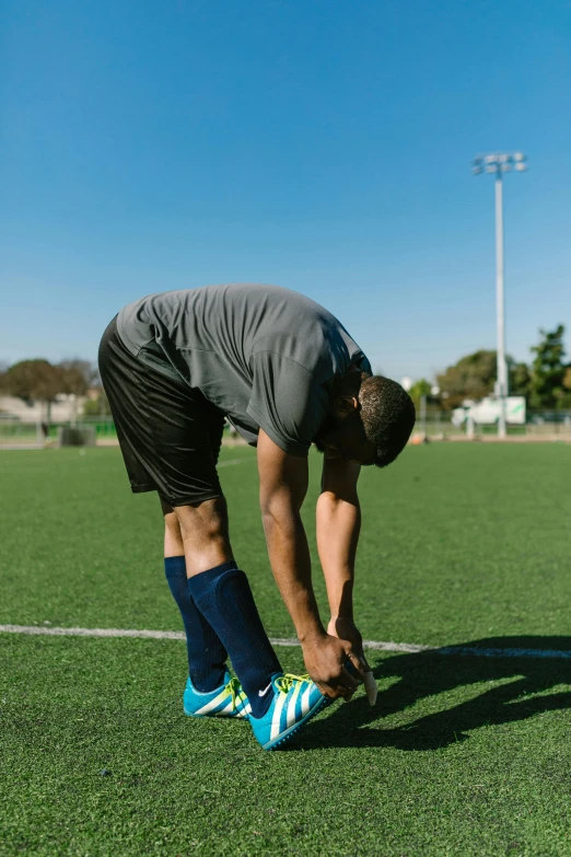 a man tying his shoe on a soccer field, arched back, compression, bay area, standing posture