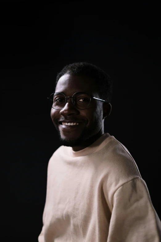 a man with glasses standing in front of a black background, hurufiyya, brown skin man with a giant grin, ignant, daniel oxford, on a pale background